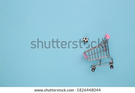Mini shopping cart with a soccer ball on a blue background. Top view
