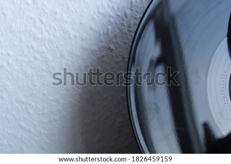 Shiny black vinyl record against a plain white textured wall 