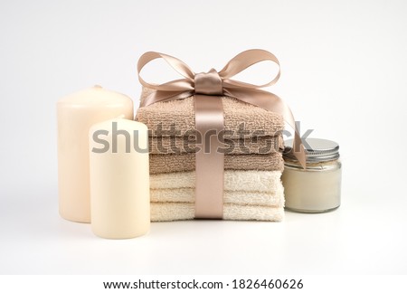 Spa set of beige and white towels tied with a satin ribbon, candles and cream, on a white background. Gift set, side view horizontal orientation. Concept of Spa treatments. Royalty-Free Stock Photo #1826460626