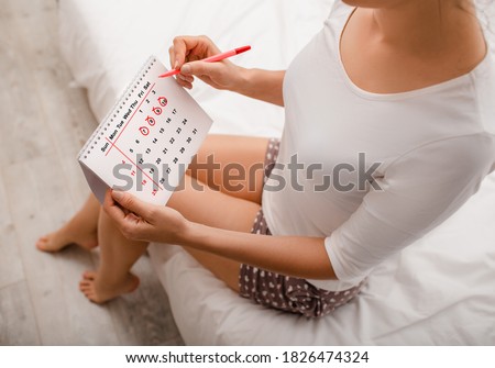 Woman planning her monthly menstruation calendar, mark the days of menstruation and ovulation. She sitting on bed wearing home clothes Royalty-Free Stock Photo #1826474324