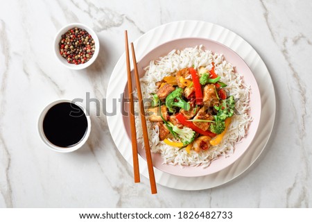 Japanese dish katsu chicken curry with vegetables: broccoli, red and yellow sweet pepper and parsley over jasmine rice served on a pink plate on a stone background served with chopsticks, close-up Royalty-Free Stock Photo #1826482733