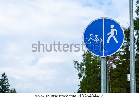 Blue sign on the pole of a pedestrian and Bicycle path against the background of blue sky and tree leaves.