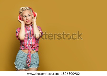 Pin-up woman listening music. Pretty model with headphones on yellow background