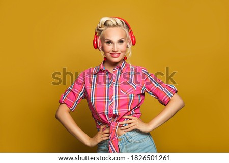 Happy blonde pin-up model woman listening music with headphones on yellow background