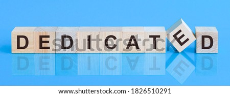 Text DEDICATED on wood cube block, stock investment concept. The text DEDICATED is written on the cubes in black letters, the cubes are located on a blue glass surface. Royalty-Free Stock Photo #1826510291