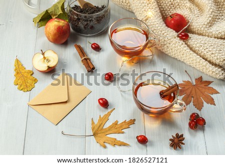 Two cups of fragrant tea with rose hips and spices on light boards, with a garland, apples and dry leaves
