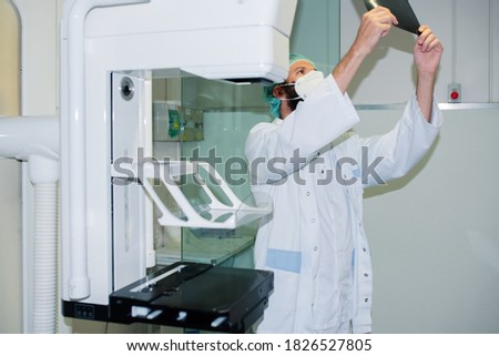 Doctor with mask checking mammography of woman in x-ray room.