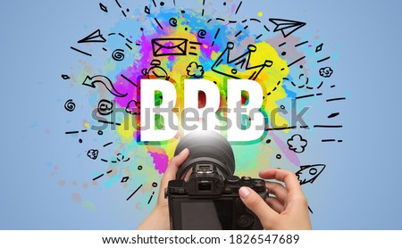 Close-up of a hand holding digital camera with abstract drawing and BRB inscription