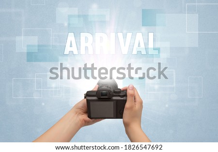 Close-up of a hand holding digital camera with ARRIVAL inscription, traveling concept
