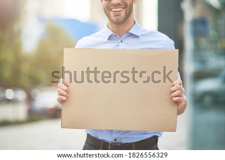 Close up shot of a smiling male activist wearing blue shirt and eyeglasses holding empty sign board while protesting outdoors