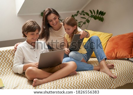 Watching cartoons online. Young beautiful caucasian family, mother and two cute little kids relaxing on sofa together and looking at laptop screen