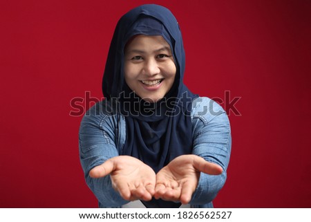Portrait of Asian muslim lady wearing hijab smiling and shows something in her empty hands, presenting offering copy space template concept