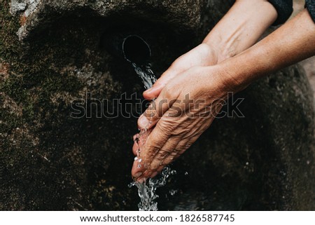 An old woman washing her hands close up of the hands in a source font with natural water