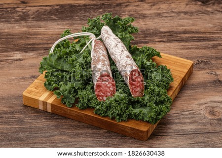 Spanish Fuet sausage with salad leaves over wooden background