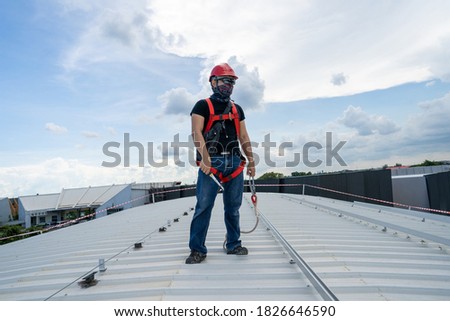 strong look man wear sunglasses red hardhat black shirt blue jeans sneaker and hardness safety belt holding wrench working on metal sheet rooftop in beautiful day stock photo