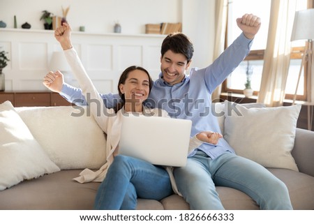 That is it! Happy laughing young married couple millennial family husband and wife sitting on sofa at home with laptop feeling excited joyful receiving good news, purchasing tour on vacation of dream Royalty-Free Stock Photo #1826666333