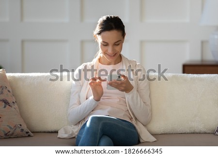 Moments for myself. Calm millennial girl with happy smile relaxing on couch using mobile phone, glad young female spending time on sofa with cell texting, chatting, playing online game, making call