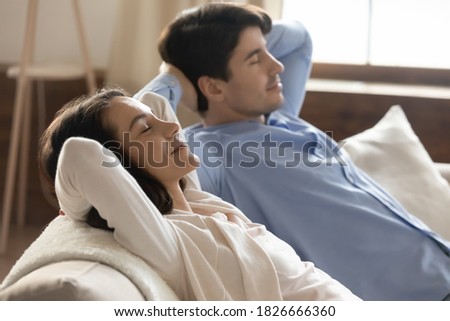 Lazy time. Beautiful serene student couple married young man and woman napping on couch with hands behind head enjoying relax and peace, millennial husband and wife reducing stress after working day Royalty-Free Stock Photo #1826666360