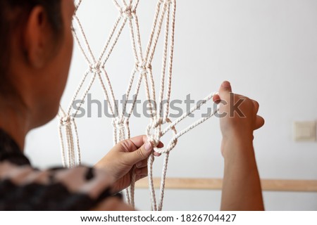 young spanish girl on her back in her bed knotting rope cross in macrame curtain, white background