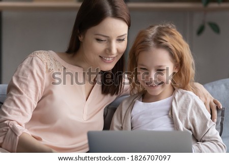 Close up smiling young woman with little girl using laptop at home, happy positive beautiful mother and adorable preschool daughter looking at computer screen, browsing apps, watching video