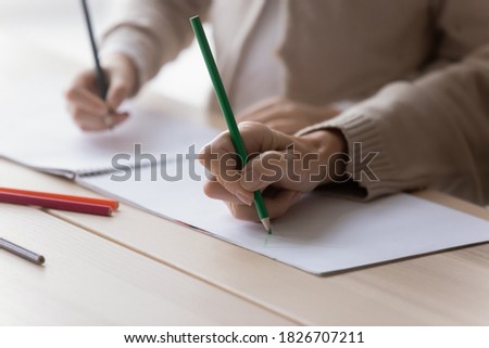 Close up mature grandmother and little girl drawing colored pencils in album together, sitting at desk at home, elderly woman babysitter and preschool granddaughter engaged creative activity