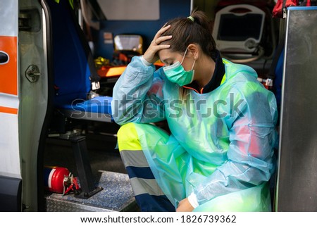 Portrait of a young woman doctor sitting on the ambulance resting exhausted where a first aid intervention during the Covid-19 pandemic, Coronavirus wearing a face mask - Rescue concept Royalty-Free Stock Photo #1826739362