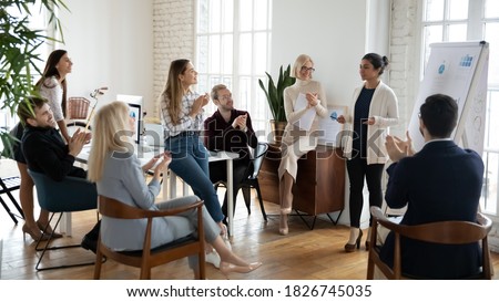 Millennial indian female trainer or team leader stand make flip chart presentation at meeting for diverse colleagues. Young woman coach lead training briefing with colleagues, present on whiteboard. Royalty-Free Stock Photo #1826745035