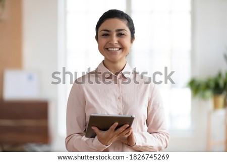 Profile picture of smiling millennial indian businesswoman hold use modern tablet gadget in office. Headshot portrait of happy young female employee consult client customer online on pad.