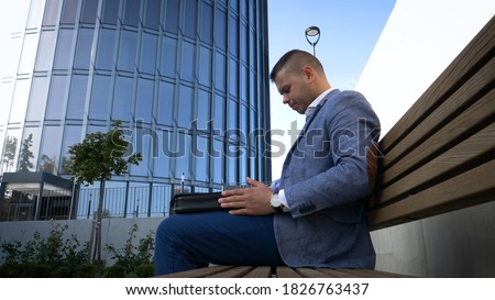 Celebrating success. Low angle view of excited young businessman keeping arms raised and expressing positivity while standing outdoors with office building in the background