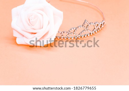 An elegant crown next to a decorative rose on pastel peach background