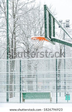  Shot of basketball basket  covered with snow on an outdoor basketball court during a snowfall in winter in the park. Healthy lifestyle concept.