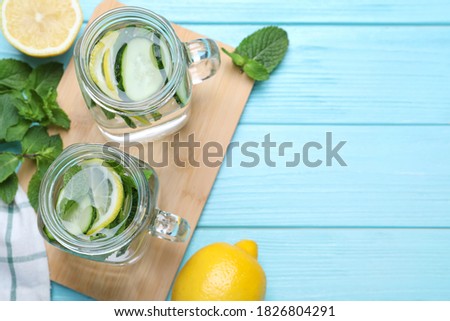 Refreshing water with cucumber, lemon and mint on light blue wooden table, flat lay. Space for text