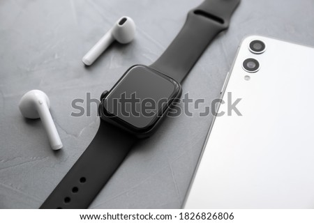 Stylish smart watch, phone and earphones on grey stone table, closeup Royalty-Free Stock Photo #1826826806