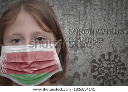 Little girl in medical mask with flag of belarus stands near the old vintage wall with text coronavirus, covid, and virus picture. Stop virus