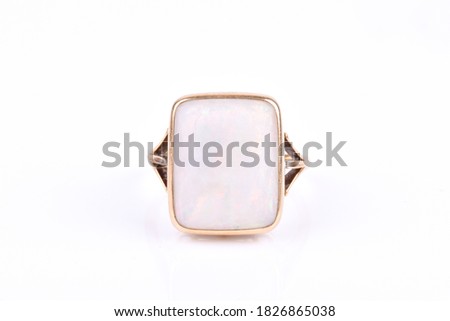 A gold ring with a large square white opal gemstone on a light background