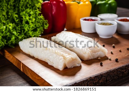 Fresh raw cod with seasonings and vegetables served on cutting board on wooden table 