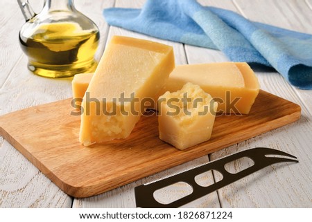 Three wedges of traditional italian hard cheese Grana Padano or Parmesan and cheese knife on a wood cutting boad near olive oil over white wood table. Front view. Royalty-Free Stock Photo #1826871224