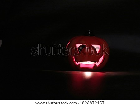 Orange ceramic Halloween pumpkin with glowing eyes and mouth lit by a t-lite candle against a dark black background