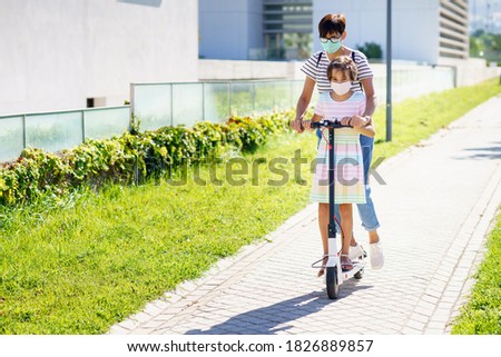 Mother and daughter riding on electric scooter in the city street.