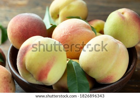Ripe peaches with leaves in a clay bowl on a wooden table. Fresh harvest.