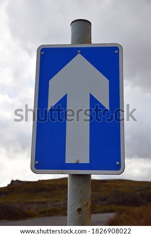 Rectangular UK blue and white one way sign with blurred background. White arrow on blue background.