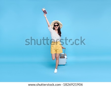 Happy young Asian tourist woman holding passport and boarding pass with baggage going to travel on holidays isolated on blue background. Royalty-Free Stock Photo #1826921906