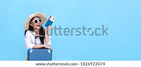 Happy young Asian tourist woman holding passport and boarding pass with baggage going to travel on holidays on blue background. Royalty-Free Stock Photo #1826922074