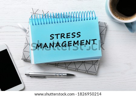Text Stress Management in notebook on white wooden table with phone and cup of coffee, flat lay