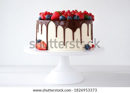 Cake with chocolate, decorated with various berries on a white table. Strawberries, blueberries, 
red currants