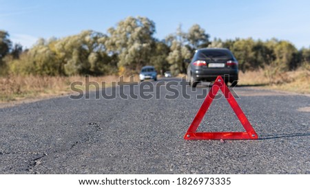 Emergency triangle stands on the road in front of cars on the background. Breakdown of the car in sunny weather. Safety of the road traffic