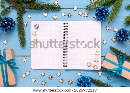 An open Notepad for writing on a blue table, with Christmas gifts.