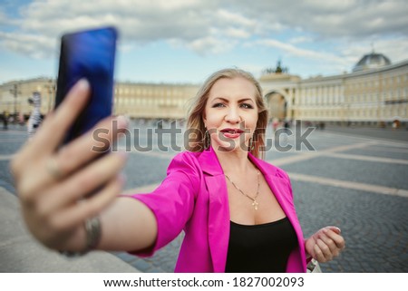 Russian woman 37 years old takes a selfie in St. Petersburg, Russia. Smiling female tourist in pink takes pictures of herself using a smartphone.