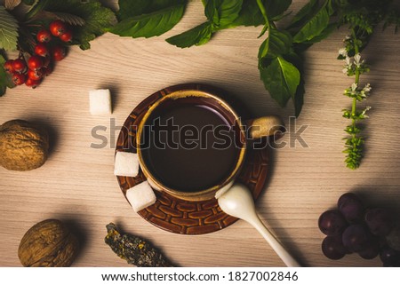 A Cup of coffee with milk is on a brown saucer. On the table are two walnuts, green Basil leaves, grapes and Rowan. The autumn atmosphere and the comfort of home create warmth and comfort.