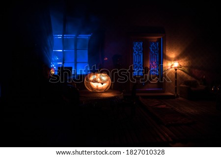 Halloween horror concept with glowing pumpkin. A realistic dollhouse living room with furniture, door and window at night. Scary zombies outside. Selective focus.